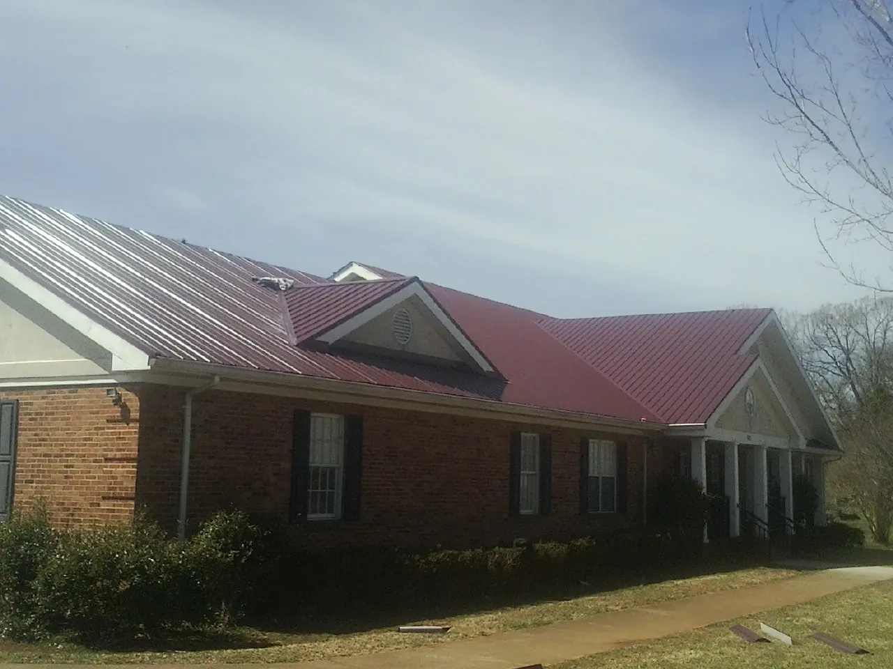 Red metal roof with gabled entries on a long brick building, from a Hail Damage Roof Repair job in Eureka